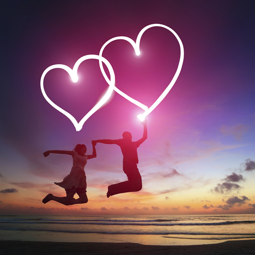 couple-with-glowing-hearts-jumping-at-beach-after-sunset